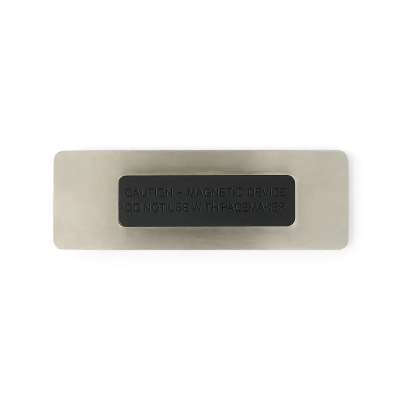 Reverso del name tag plateado con la pieza magnética negra montada y texto de advertencia en relieve
